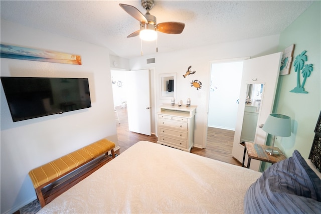 bedroom with a textured ceiling, wood-type flooring, and ceiling fan