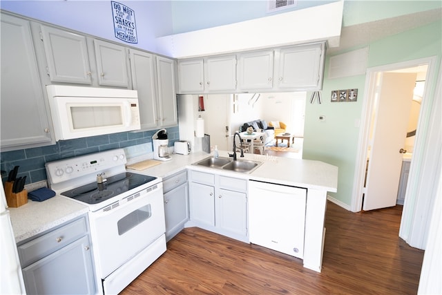 kitchen with kitchen peninsula, dark hardwood / wood-style flooring, sink, and white appliances