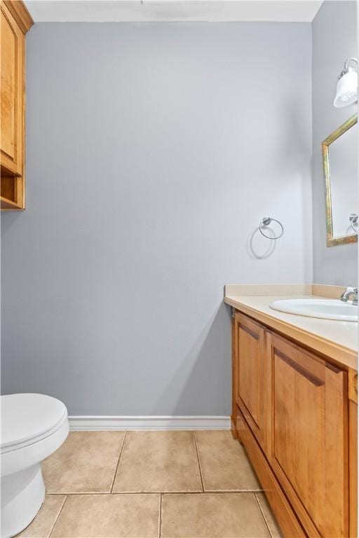 half bath with baseboards, tile patterned flooring, toilet, and vanity