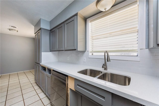 kitchen with tasteful backsplash, light tile patterned floors, gray cabinets, stainless steel dishwasher, and a sink