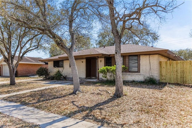 ranch-style house featuring an attached garage, fence, and brick siding