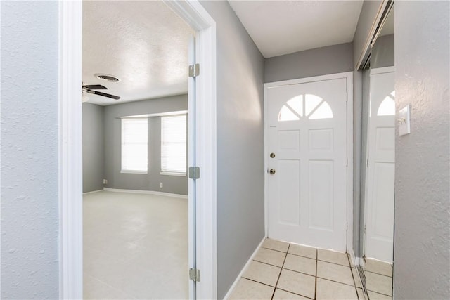 foyer with light tile patterned floors, a ceiling fan, visible vents, baseboards, and a textured ceiling