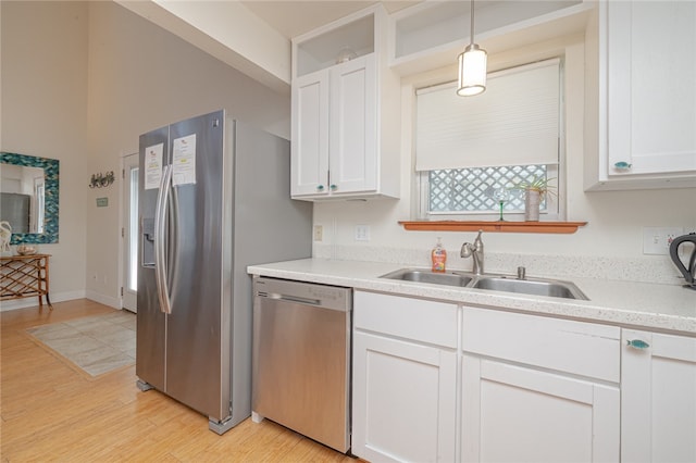 kitchen featuring stainless steel appliances, hanging light fixtures, sink, white cabinets, and light hardwood / wood-style flooring