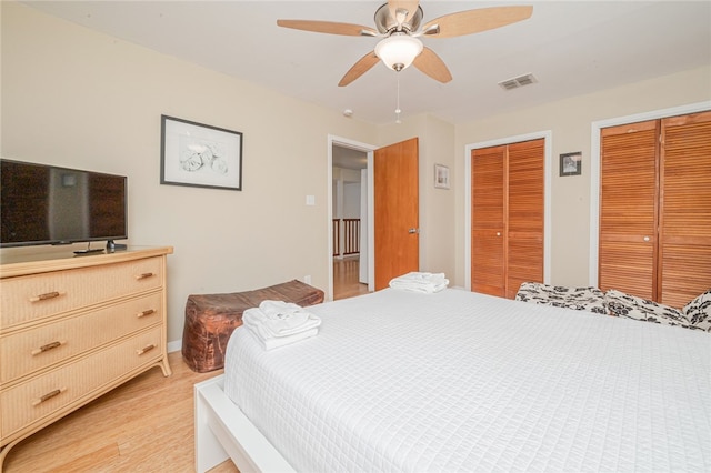 bedroom featuring ceiling fan, light hardwood / wood-style flooring, and two closets