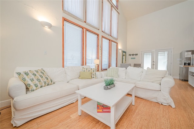 living room with french doors, high vaulted ceiling, plenty of natural light, and light hardwood / wood-style floors