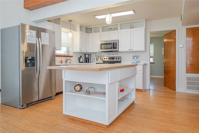 kitchen featuring a center island, white cabinetry, appliances with stainless steel finishes, hanging light fixtures, and light hardwood / wood-style flooring