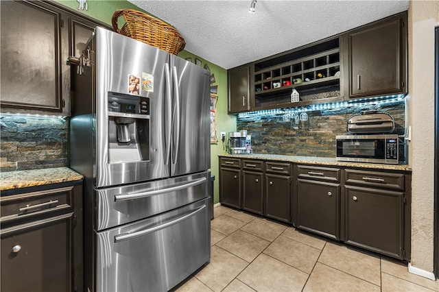 kitchen with backsplash, appliances with stainless steel finishes, a textured ceiling, dark brown cabinets, and light tile patterned floors