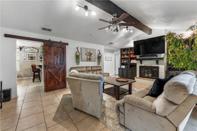 living room with a textured ceiling, lofted ceiling with beams, a barn door, and light tile patterned flooring