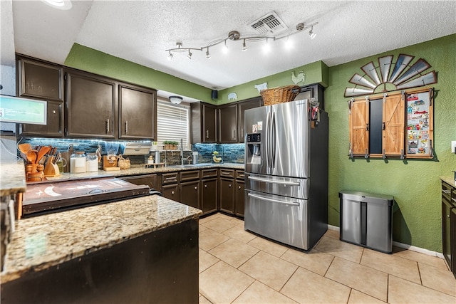 kitchen with dark brown cabinetry, a textured ceiling, light stone counters, and stainless steel fridge