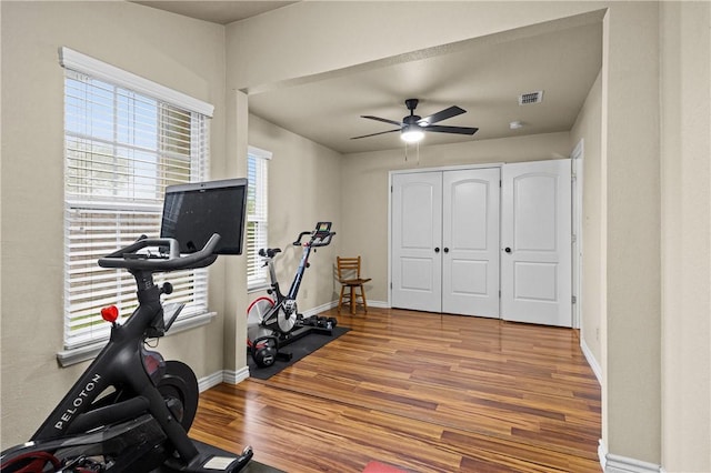 exercise room featuring baseboards, ceiling fan, visible vents, and wood finished floors
