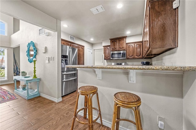 kitchen featuring visible vents, a peninsula, a kitchen breakfast bar, light wood-style flooring, and stainless steel appliances