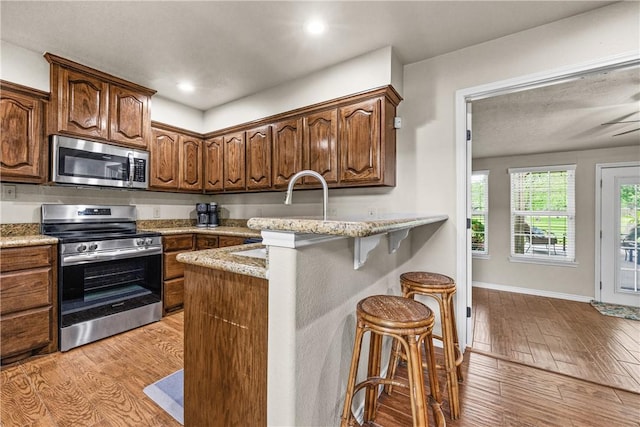 kitchen with a kitchen bar, appliances with stainless steel finishes, light wood-type flooring, baseboards, and light stone counters