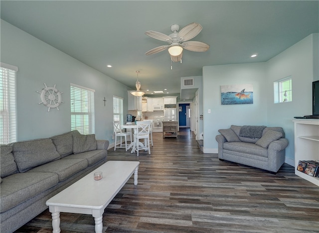 living room with dark wood-type flooring, ceiling fan, and a healthy amount of sunlight