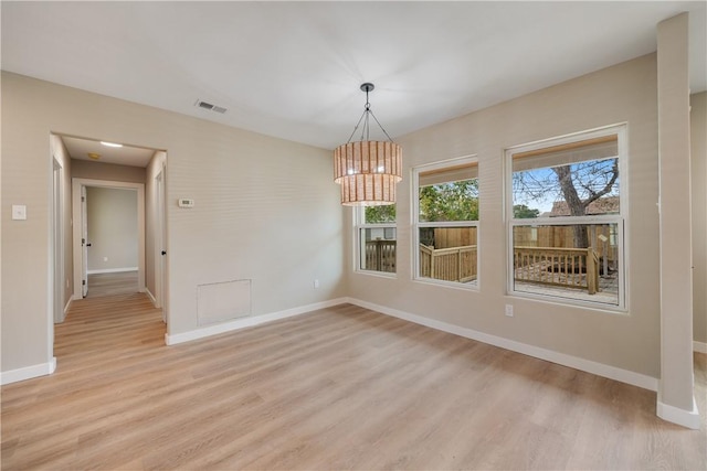 unfurnished dining area featuring an inviting chandelier and light hardwood / wood-style floors