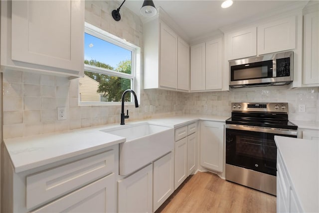 kitchen with sink, white cabinetry, appliances with stainless steel finishes, light hardwood / wood-style floors, and decorative backsplash