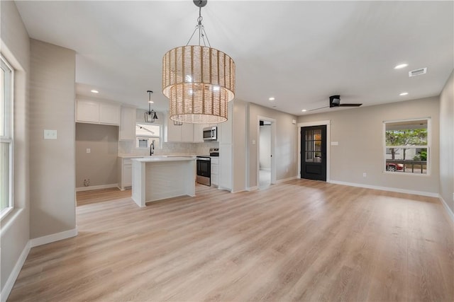 unfurnished living room featuring sink, light hardwood / wood-style floors, and ceiling fan with notable chandelier