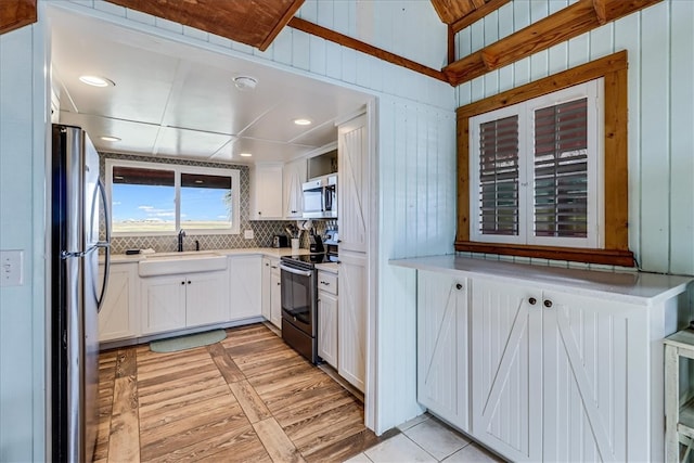 kitchen featuring white cabinets, appliances with stainless steel finishes, wooden walls, and light hardwood / wood-style flooring