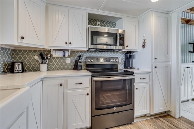 kitchen with white cabinetry, decorative backsplash, appliances with stainless steel finishes, and light hardwood / wood-style floors