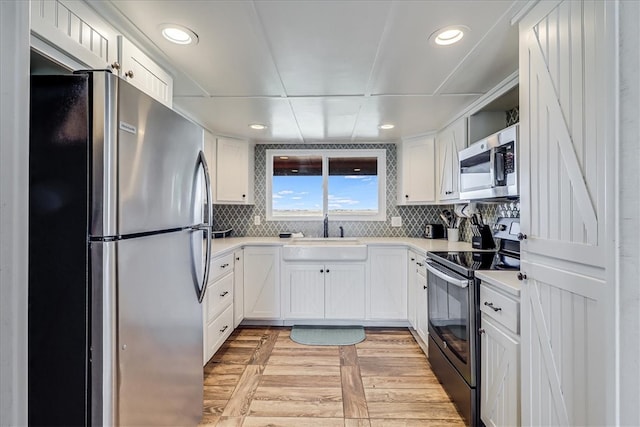 kitchen with stainless steel appliances, white cabinetry, sink, tasteful backsplash, and light hardwood / wood-style flooring