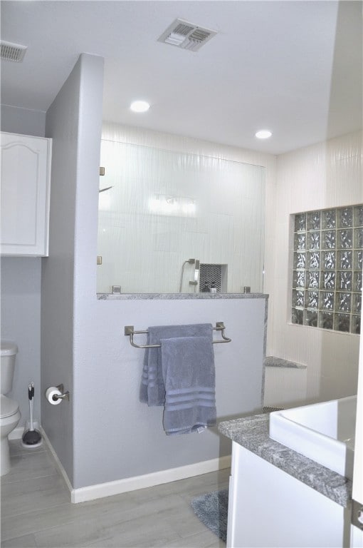 bathroom with hardwood / wood-style flooring, vanity, toilet, and a shower