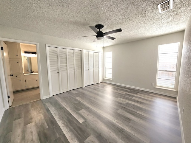 unfurnished bedroom featuring ensuite bathroom, dark hardwood / wood-style flooring, a textured ceiling, and ceiling fan