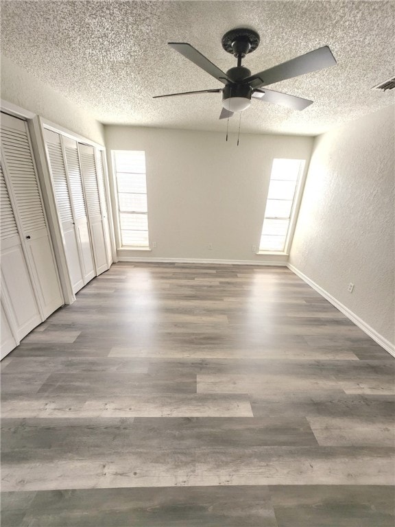 unfurnished bedroom featuring two closets, ceiling fan, dark hardwood / wood-style flooring, and a textured ceiling