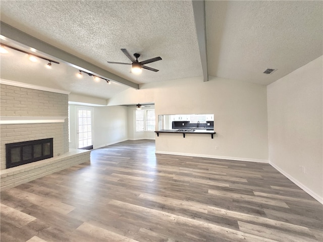 unfurnished living room featuring a textured ceiling, dark hardwood / wood-style flooring, a brick fireplace, and vaulted ceiling with beams