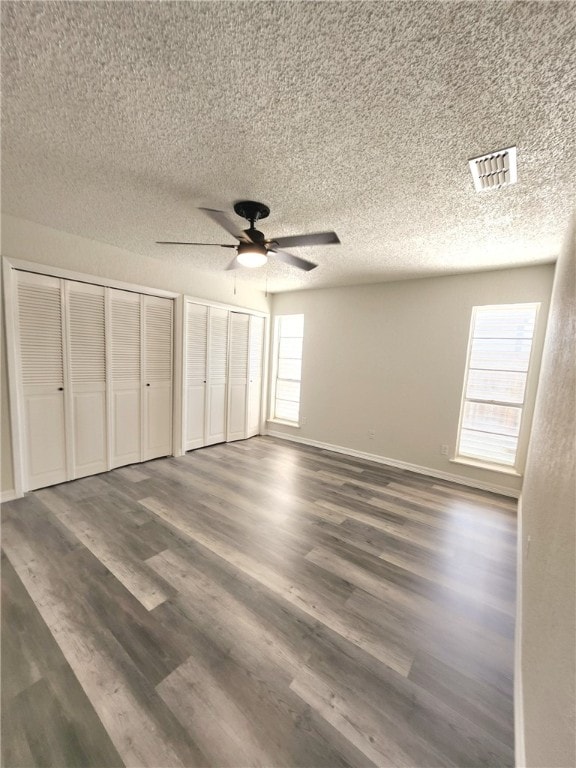 unfurnished bedroom featuring dark hardwood / wood-style flooring, two closets, ceiling fan, and a textured ceiling