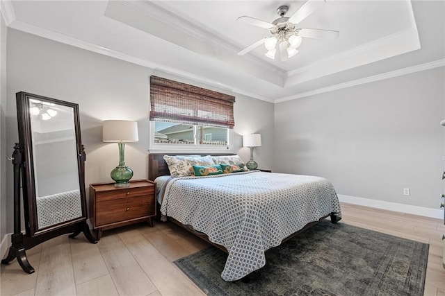 bedroom with ornamental molding, a tray ceiling, and light wood-style flooring