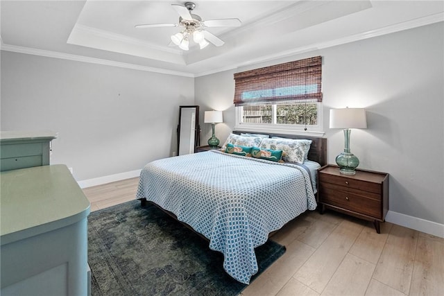 bedroom featuring crown molding, baseboards, a raised ceiling, and light wood-style floors