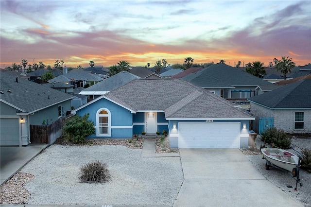 ranch-style home featuring a garage, fence, concrete driveway, a residential view, and stucco siding