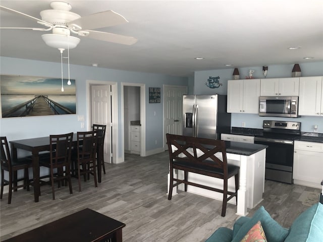 kitchen with appliances with stainless steel finishes, white cabinetry, ceiling fan, and hardwood / wood-style floors