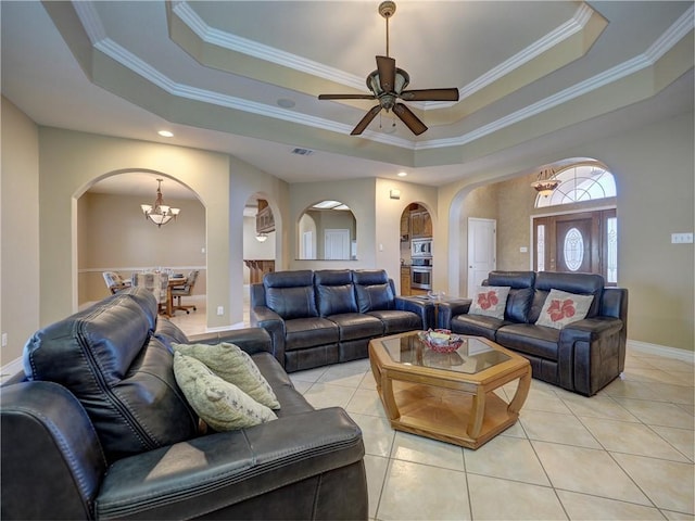 living area featuring light tile patterned floors, a raised ceiling, ceiling fan with notable chandelier, and arched walkways