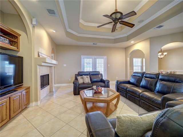 living room featuring plenty of natural light, visible vents, arched walkways, ceiling fan with notable chandelier, and a tray ceiling