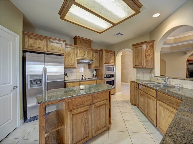 kitchen with appliances with stainless steel finishes, a sink, arched walkways, tasteful backsplash, and visible vents