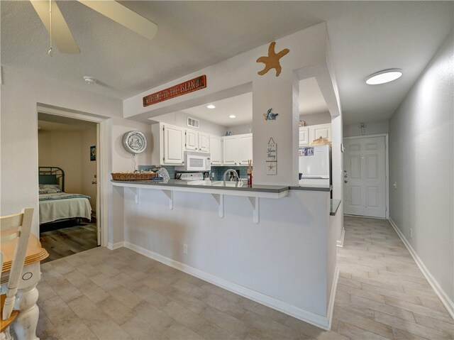 kitchen with white appliances, a breakfast bar, white cabinets, kitchen peninsula, and ceiling fan