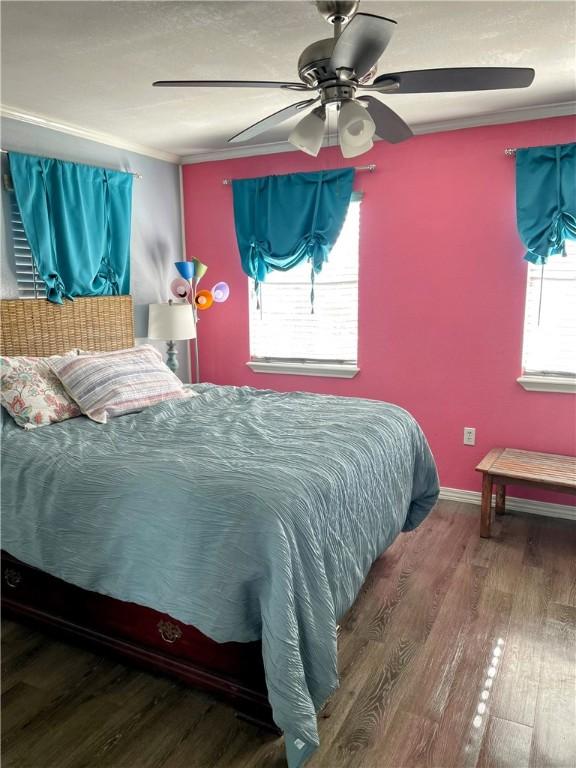 bedroom featuring multiple windows, hardwood / wood-style floors, ornamental molding, and ceiling fan