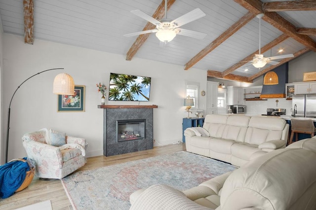 living area with light wood finished floors, baseboards, lofted ceiling with beams, ceiling fan, and a premium fireplace