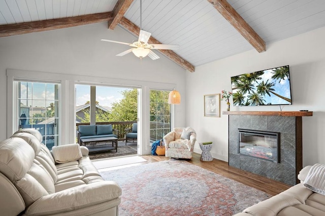 living area with vaulted ceiling with beams, ceiling fan, wood finished floors, and a tile fireplace