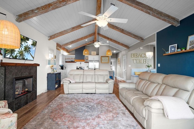 living area with baseboards, a tiled fireplace, lofted ceiling with beams, ceiling fan, and wood finished floors