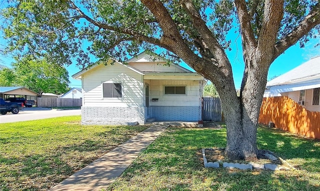 bungalow featuring brick siding, a front lawn, and fence