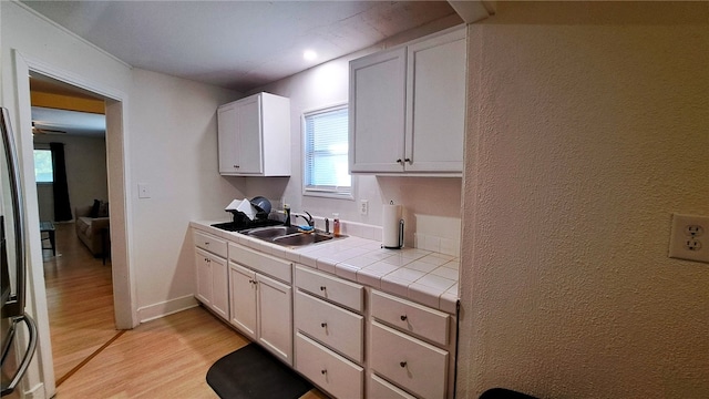 kitchen featuring baseboards, a sink, white cabinetry, light wood-style flooring, and tile countertops