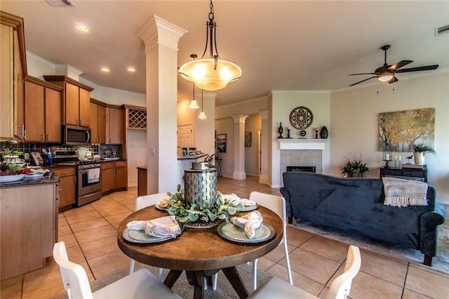 tiled dining room with ceiling fan, crown molding, ornate columns, and a fireplace