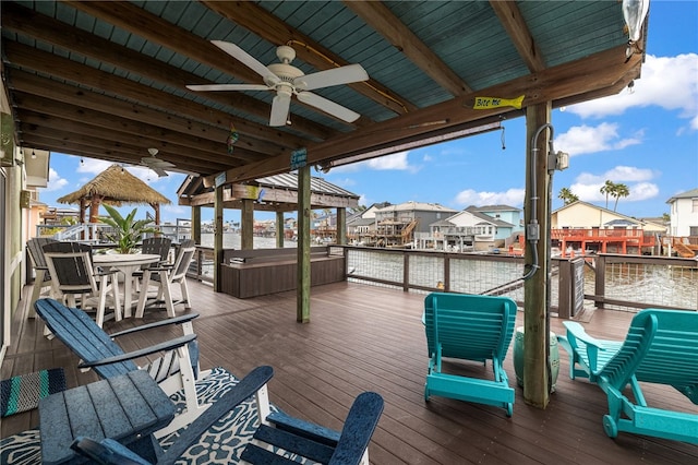 deck featuring ceiling fan, a residential view, a water view, and a hot tub