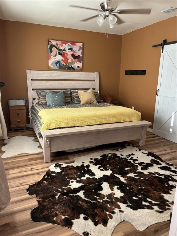 bedroom featuring light wood finished floors, visible vents, ceiling fan, and a barn door