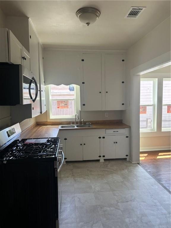 kitchen with a sink, white cabinetry, appliances with stainless steel finishes, and a healthy amount of sunlight