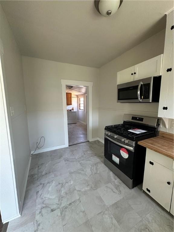 kitchen with stainless steel appliances, baseboards, white cabinetry, marble finish floor, and wood counters