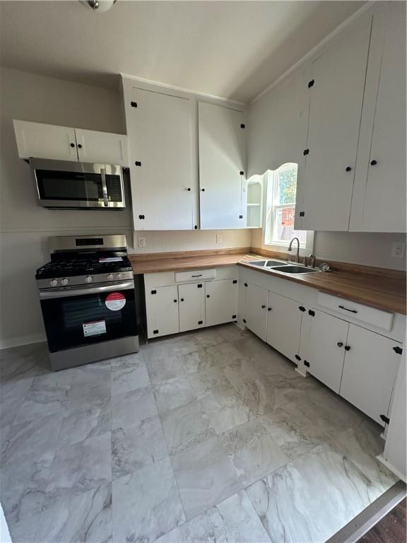 kitchen with stainless steel appliances, a sink, white cabinetry, and butcher block counters