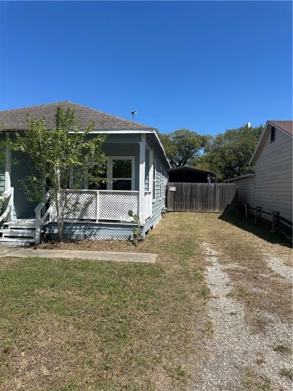 view of side of home with a lawn, fence, and roof with shingles