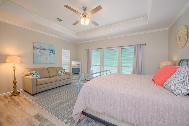 bedroom with light wood-type flooring, a raised ceiling, ceiling fan, and crown molding